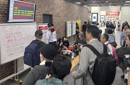 Pasajeros de una estación de tren escuchan novedades después de que el terremoto interrumpiera el servicio