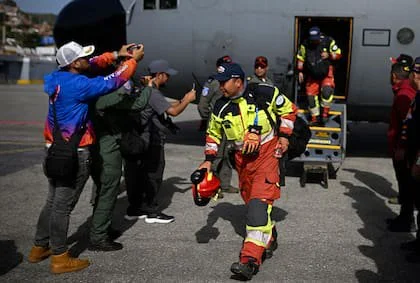 Residentes locales toman instantáneas mientras bomberos ecuatorianos del equipo de Búsqueda y Rescate Urbano (USAR) descienden del avión a su llegada al aeropuerto internacional Simón Bolívar en La Guaira, Venezuela, el 26 de junio de 2026, tras los devastadores terremotos que azotaron el país