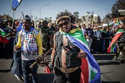 El locutor de radio sudafricano y líder de grupo Ngizwe Mchunu (C) revisa su teléfono mientras encabeza una manifestación